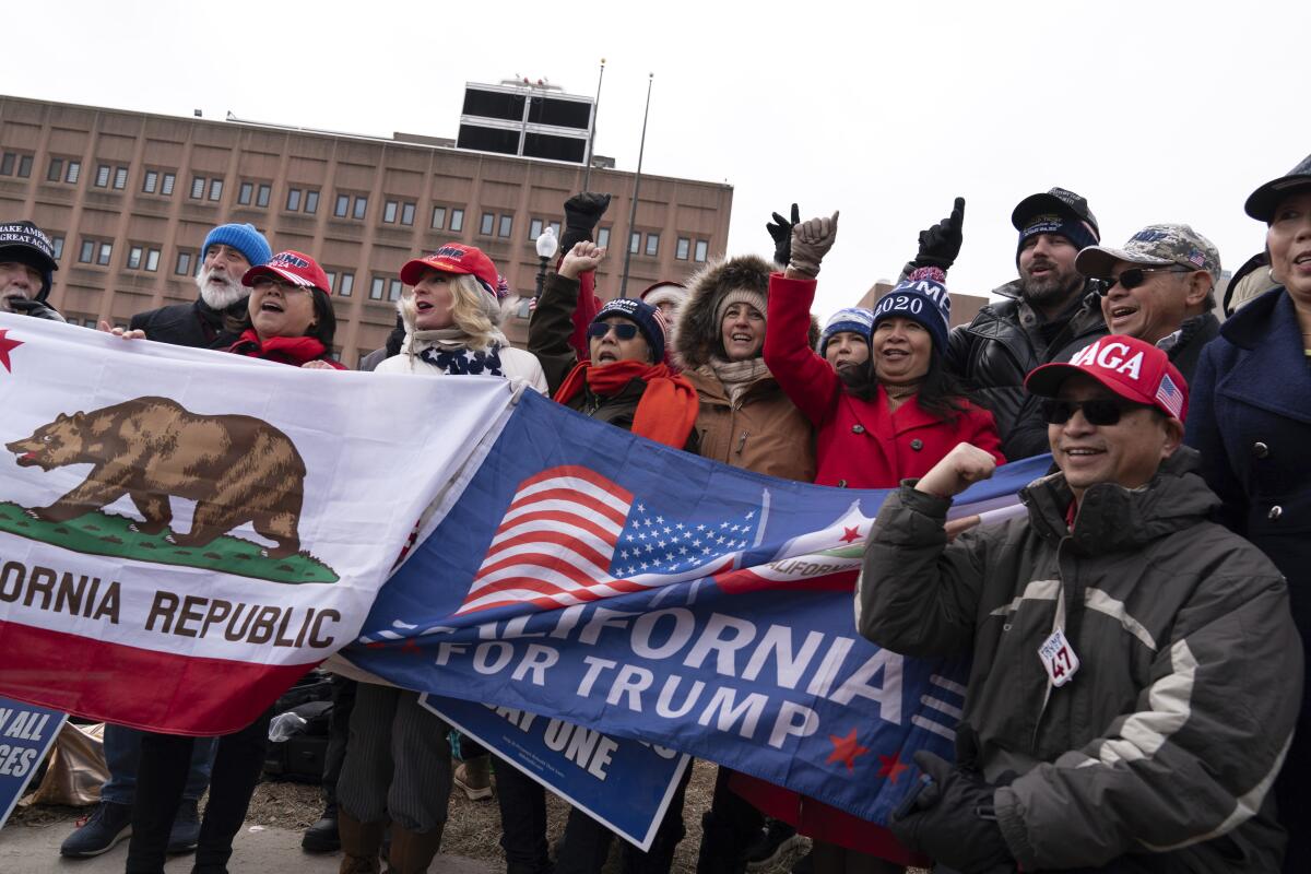 Trump supporters, some holding flags, rally near a building