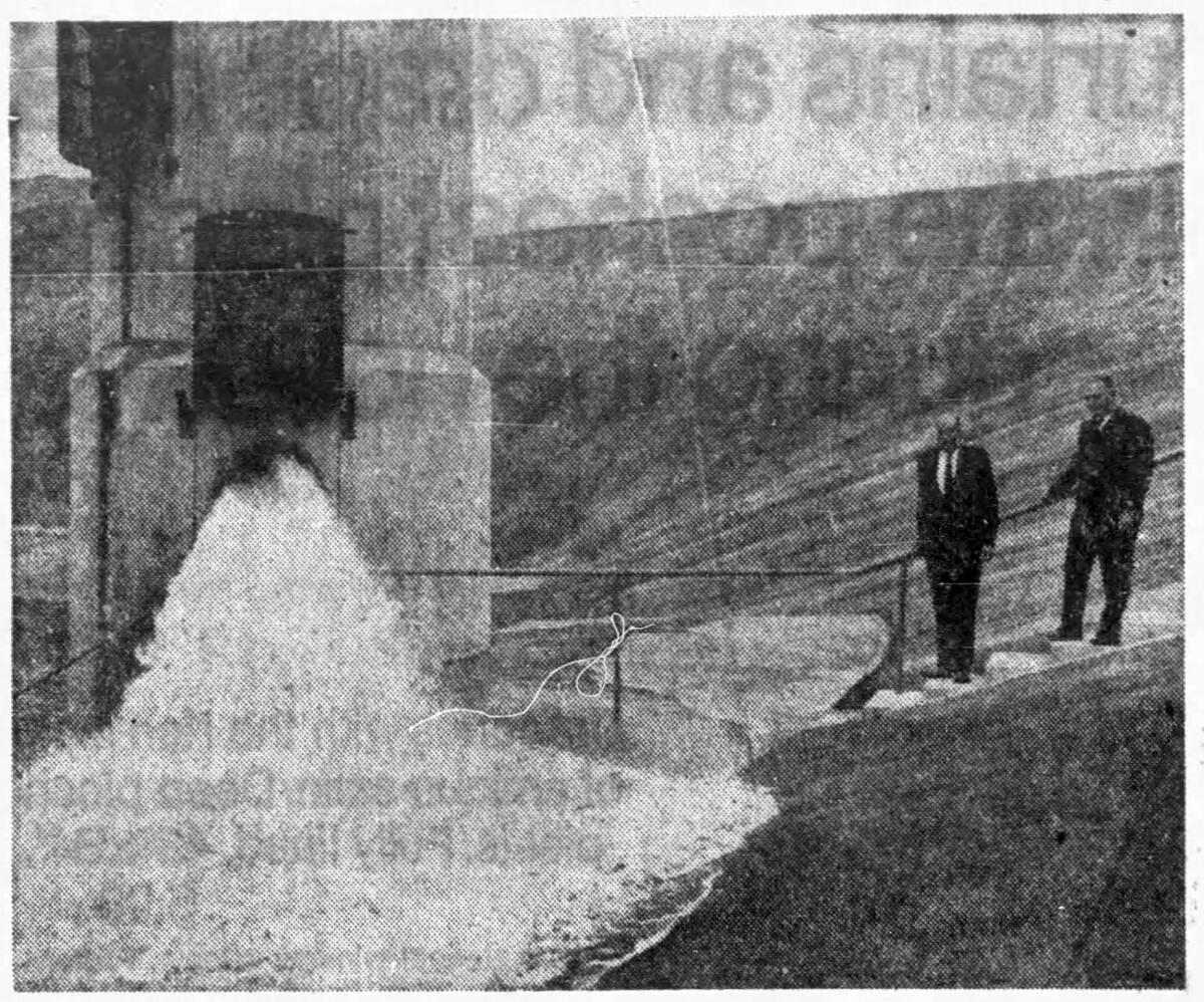 A black-and-white photo of two men standing by as a reservoir is filled 