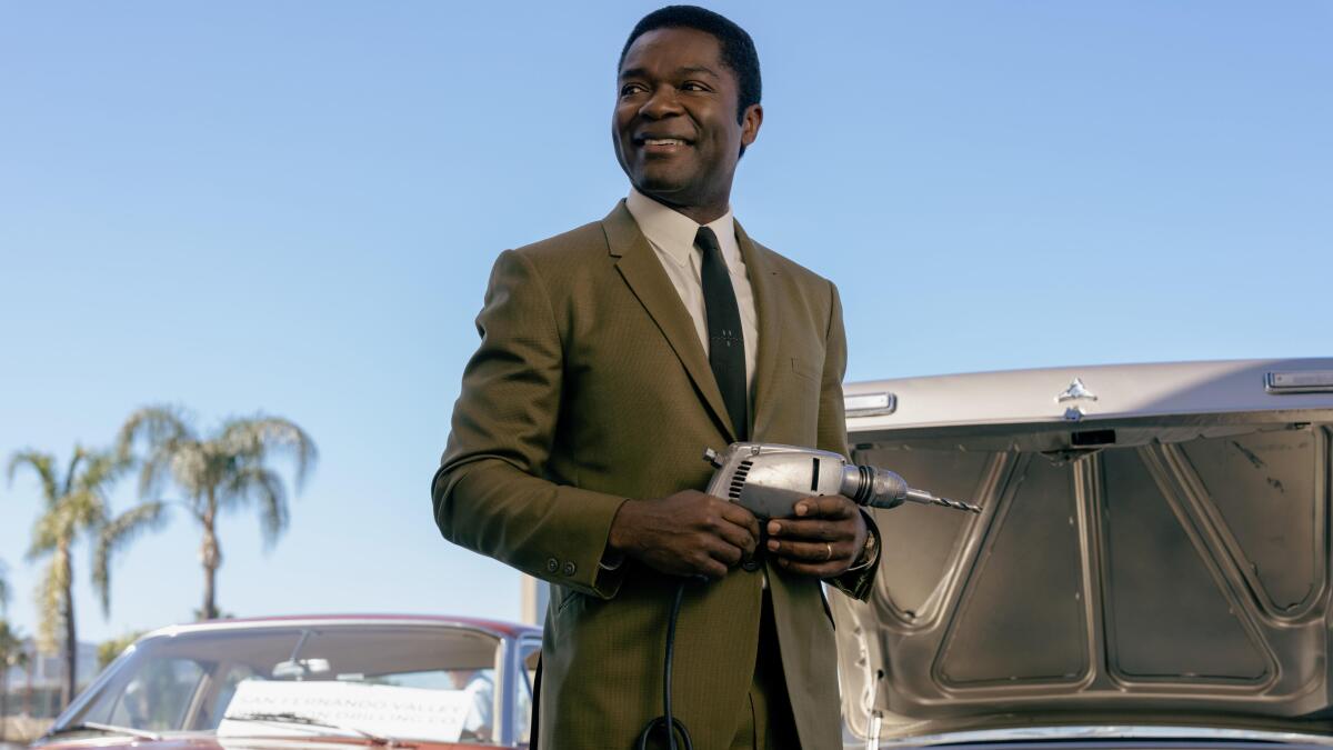 A man in a suit smiles in front of palm trees.