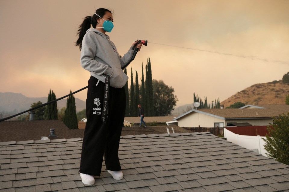 Person spraying water on a roof during a wildfire.