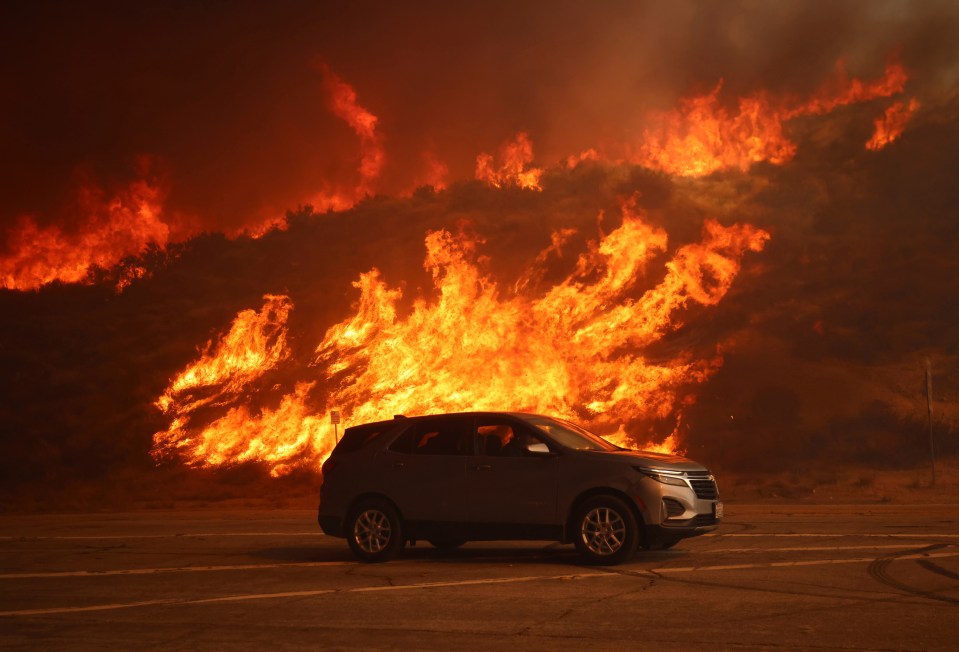 SUV driving past a hillside engulfed in flames.