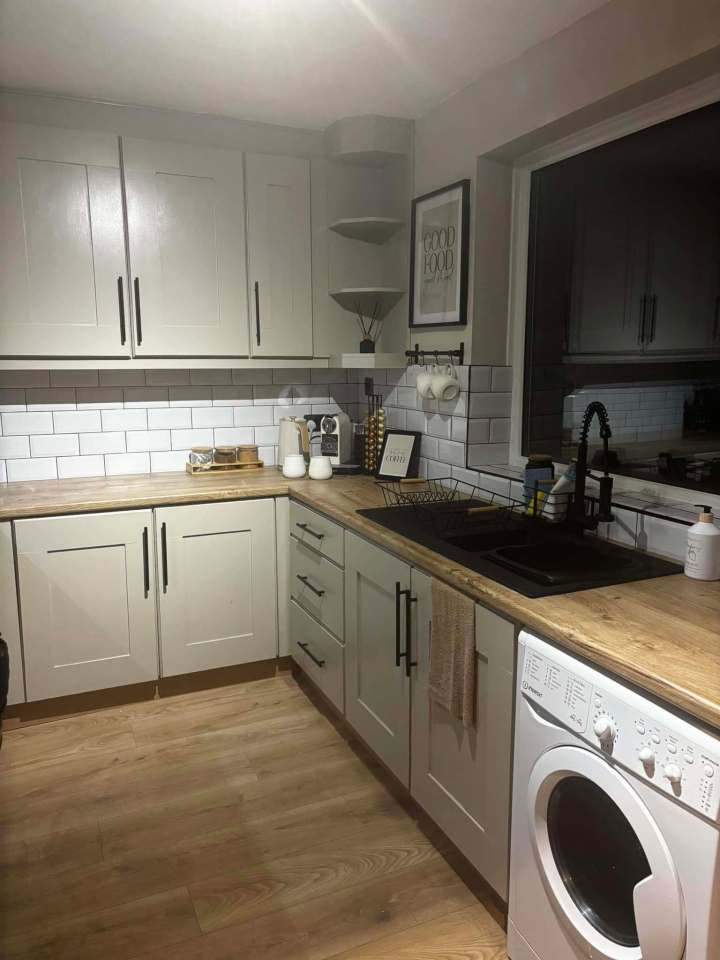 A renovated kitchen with light-colored cabinets, wood countertops, and white subway tile backsplash.