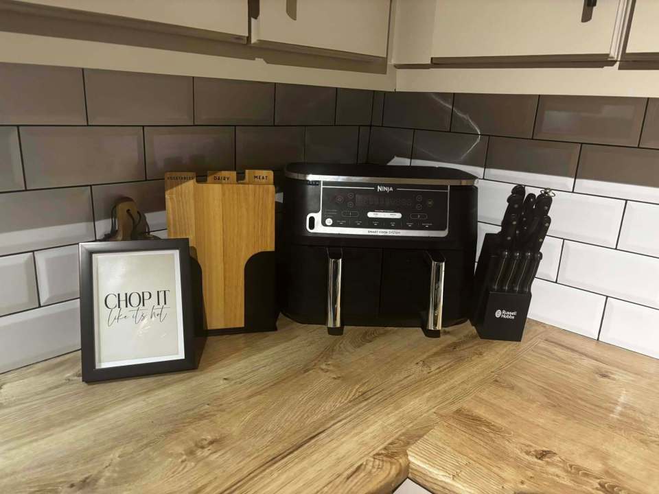 Kitchen countertop with Ninja air fryer, knives, cutting board, and framed print.