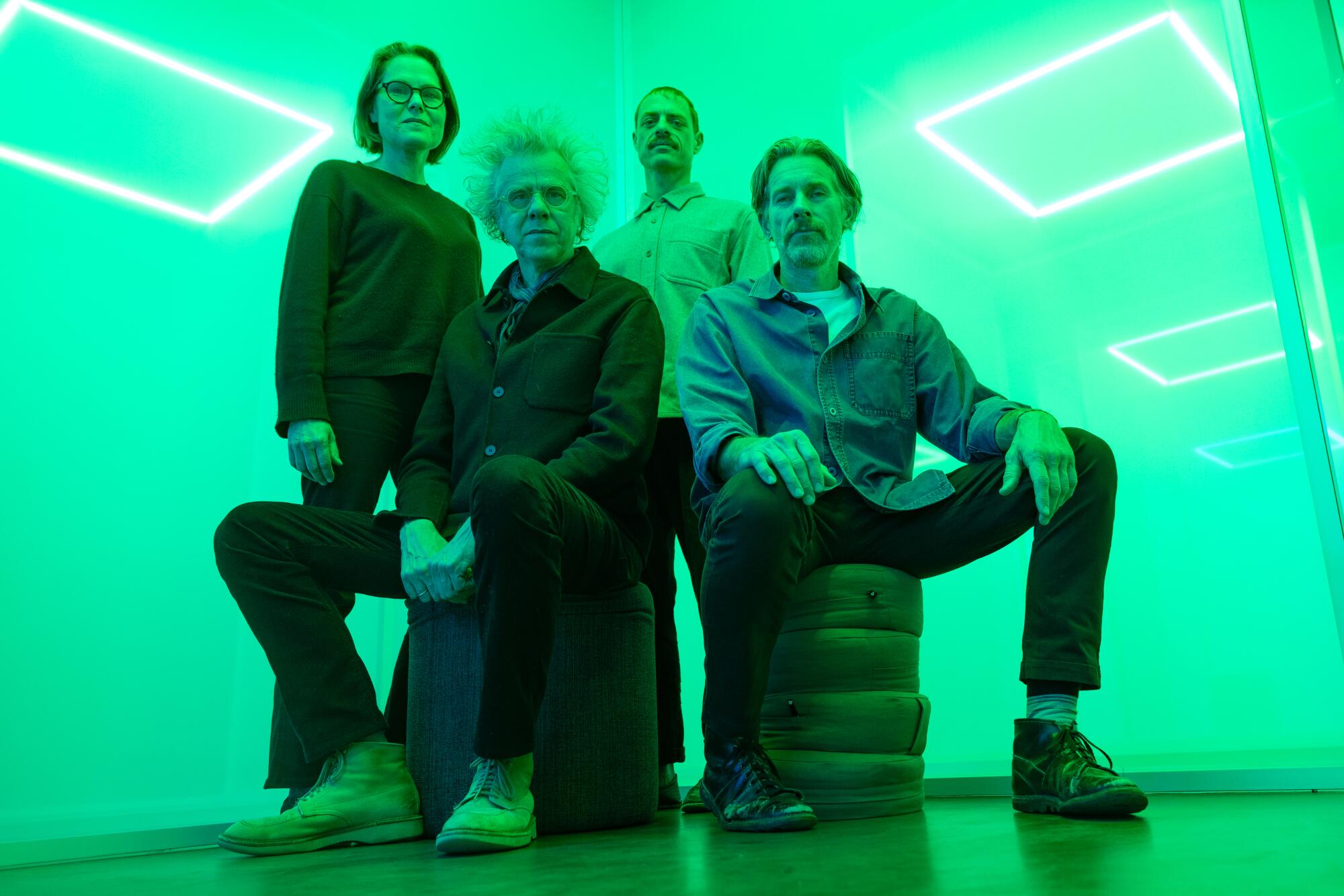 Four artists sit in front of scrims awash in a green-ish light.