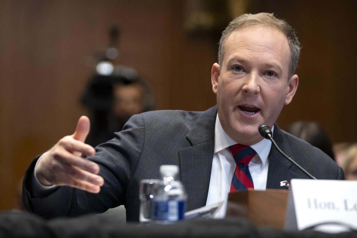 A man speaks into a microphone and gestures with his right hand.