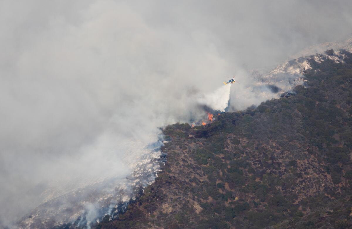 A helicopter makes a water drop on a burning ridge in Brentwood during the Palisades fire.