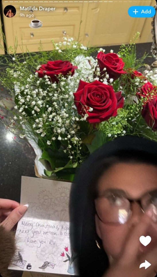 A woman holding a card and a bouquet of red roses.