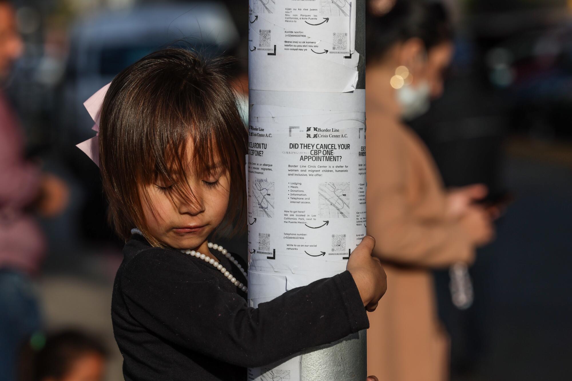 A young girl hugs a post, her eyes closed. 