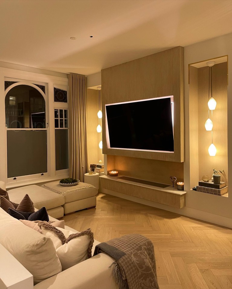 Renovated living room with large TV and herringbone floors.