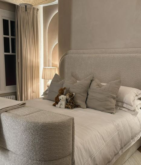 A plush, beige bedroom with stuffed animals on the bed.