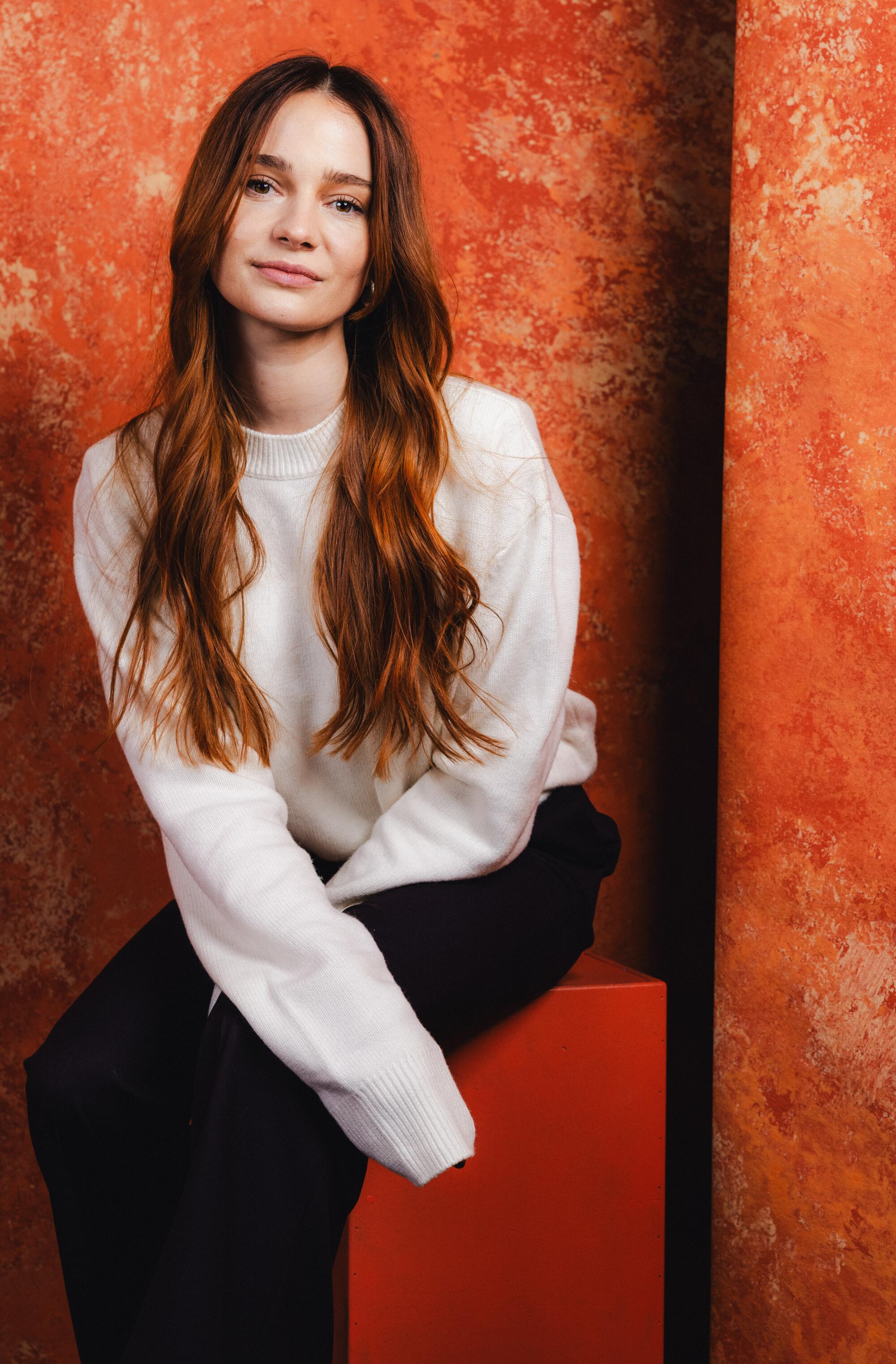 Aisling Franciosi of "Twinless" sits on an orange block in front of an orange backdrop