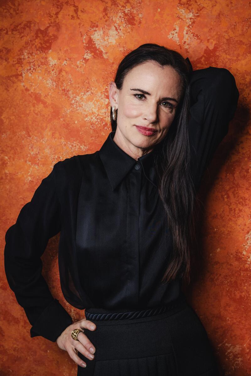 Juliette Lewis stands against an orange wall, one hand behind her head