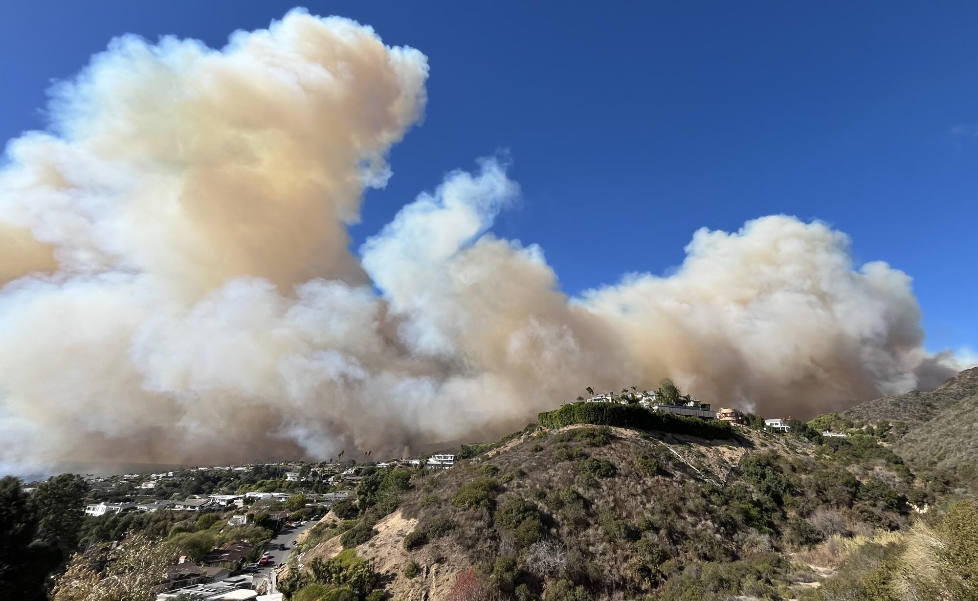 A large plume of smoke from the Palisades fire rises over the ridge line.