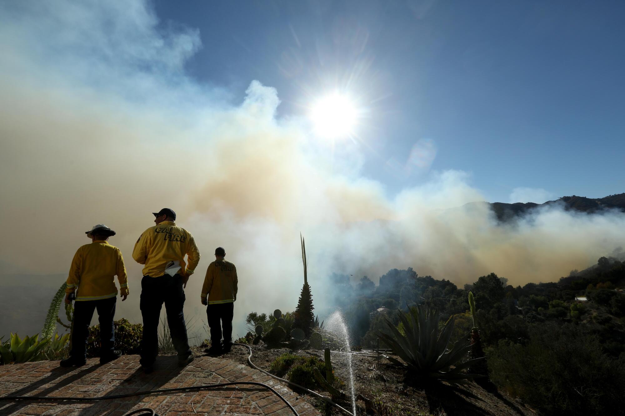 Firefighters on a hillside patio monitor an approaching fire.