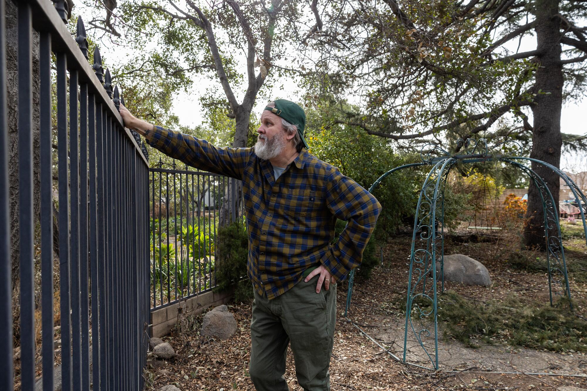 A man stands at a wrought iron fence in a yard.