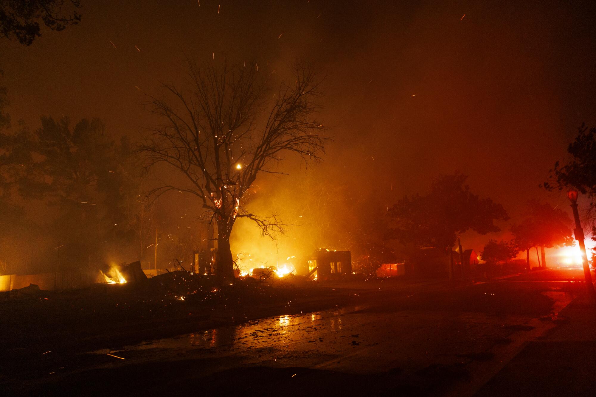 The orange glow of fire lights the night sky along a suburban street at night.