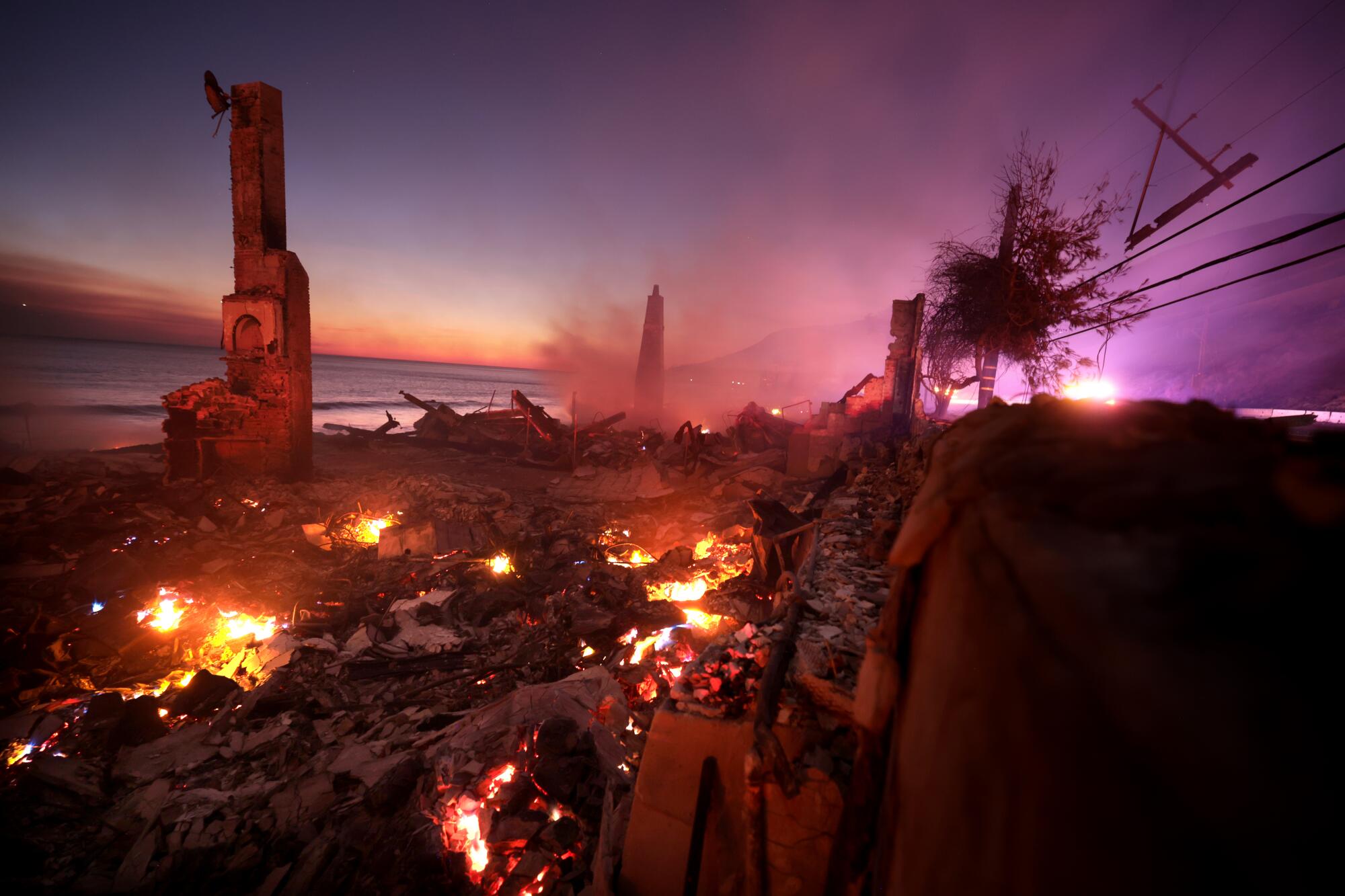 Hot spots glow red in the remains of a house, a chimney still standing.