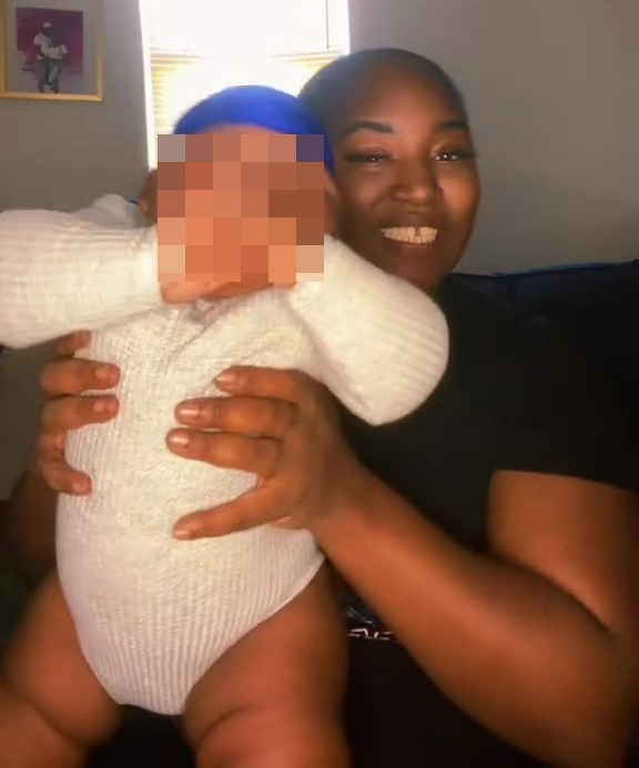 A woman holding a baby wearing a blue hat.  The baby's face is blurred.