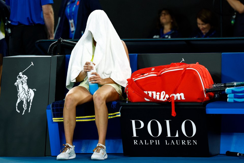 Aryna Sabalenka sits dejected, covered by a towel, after a tennis match.