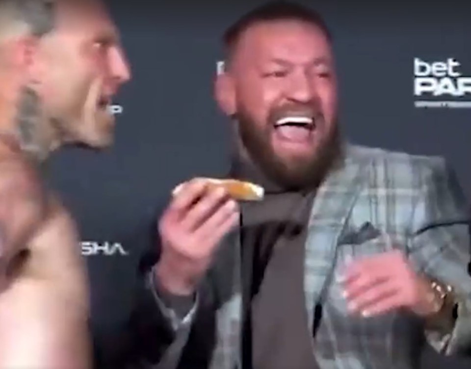 Man eating a pastry while laughing next to another man.