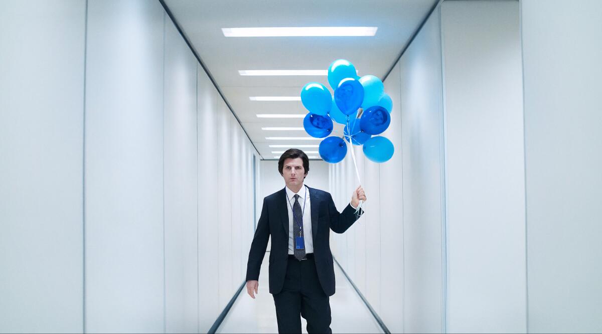 A man in a suit walks down a barren white hallway with blue balloons.