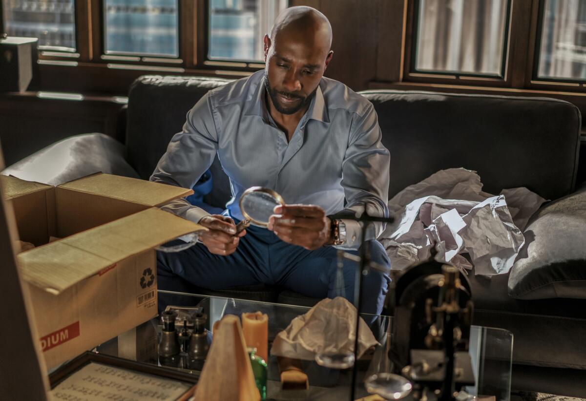 A man sits on a couch looking at a magnifying glass he's unpacked from a box.