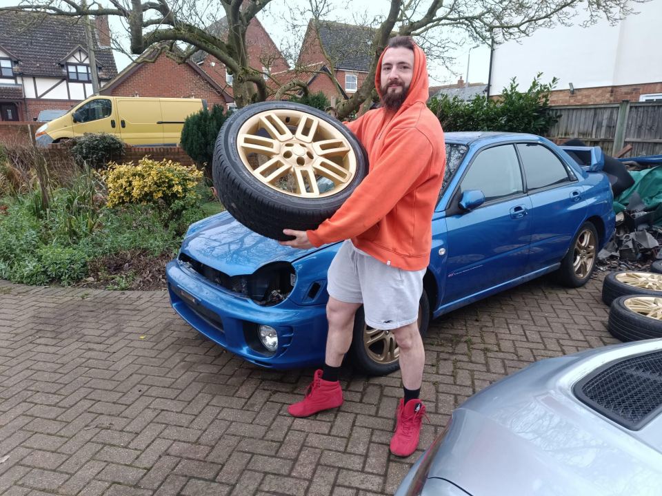 Man holding gold car rim in front of blue car.