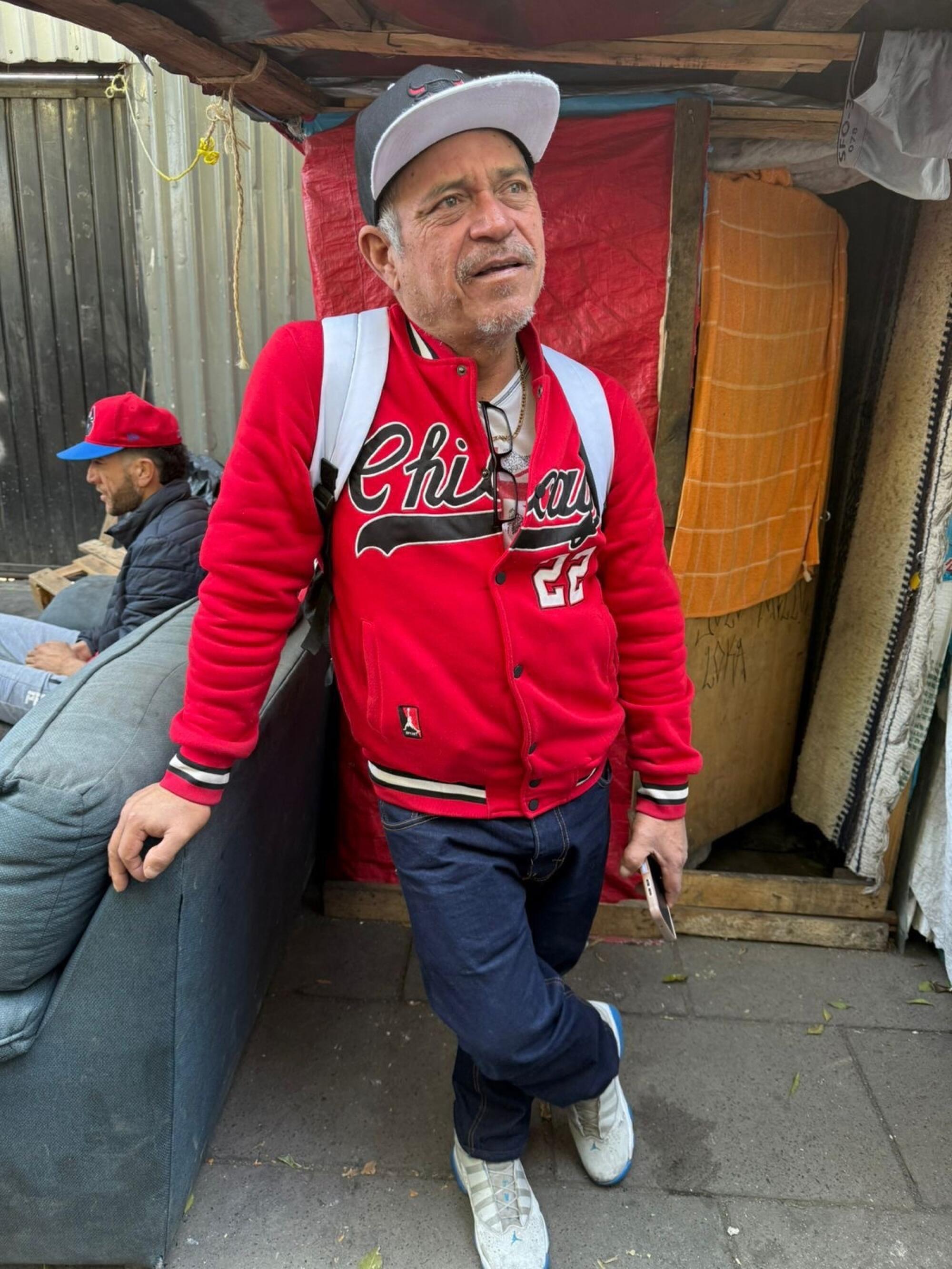 A man in a red jacket leans against a piece of furniture. 