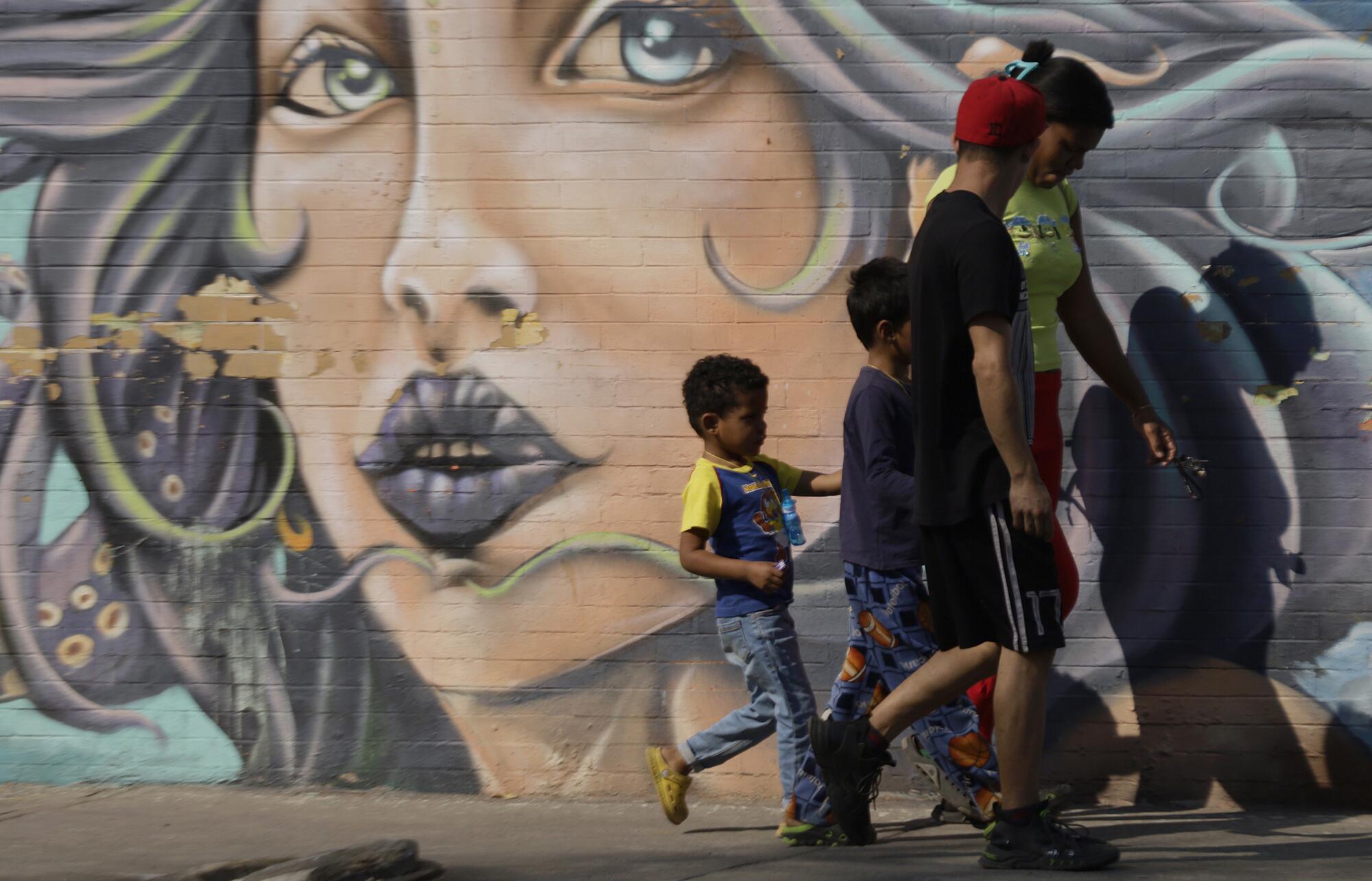 Two adults and two children walk past a mural of a woman's face.