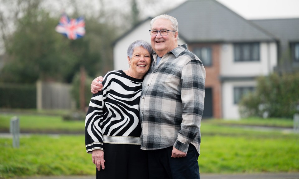 A couple smiling and embracing in front of their house.