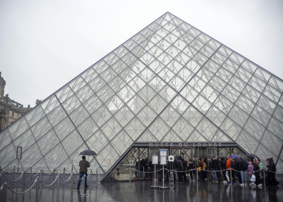 Tourists stand outside the Louvre museum's glass entrance pyramid