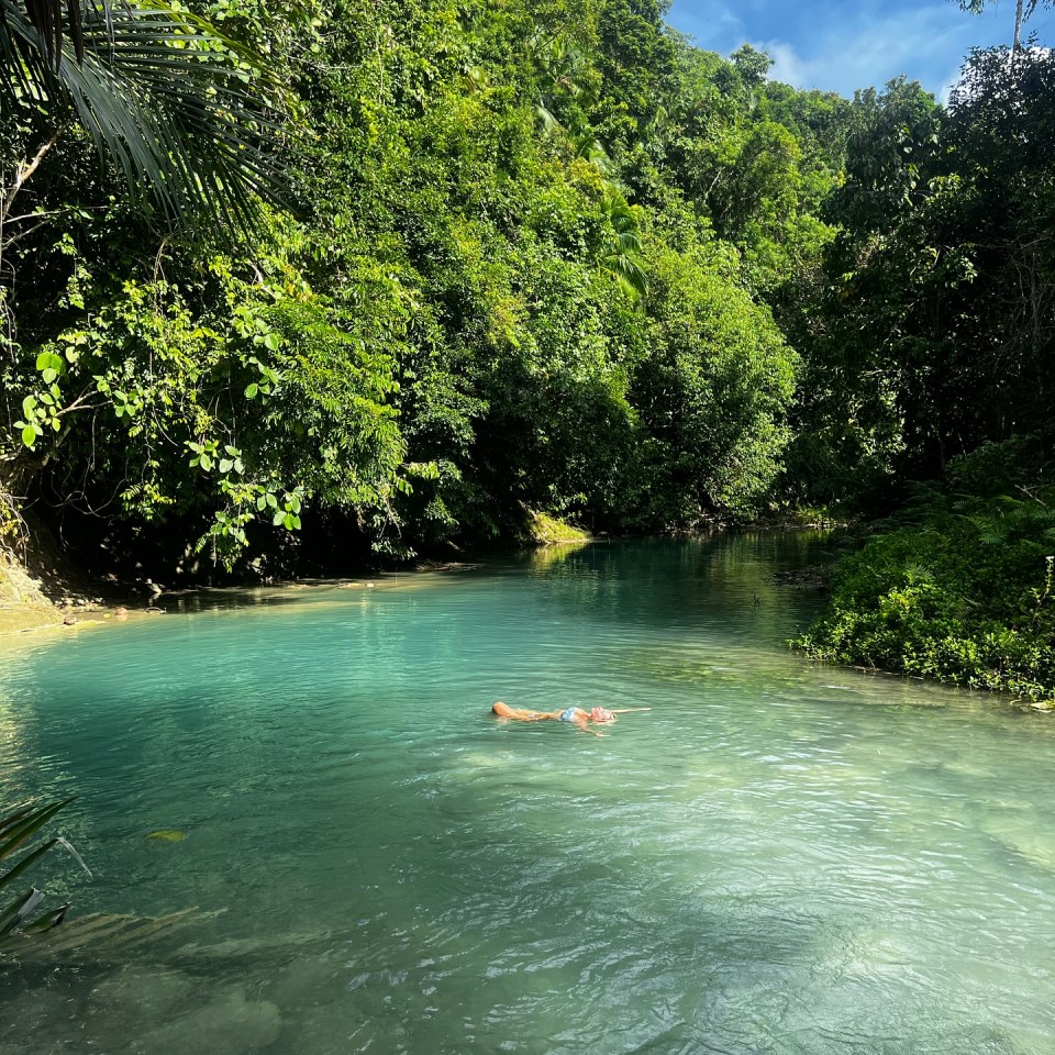 Woman floating in a calm, turquoise river surrounded by lush green vegetation.