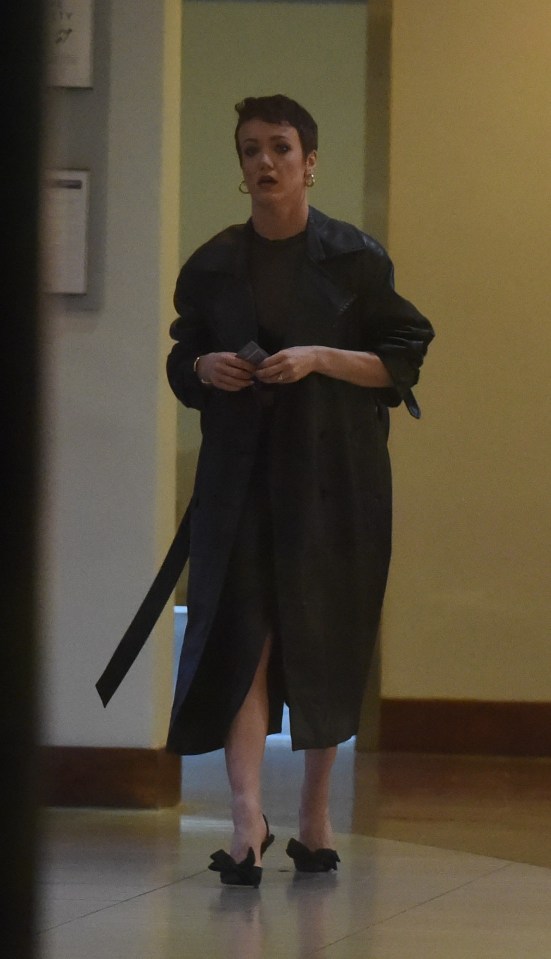 Woman in black coat and shoes walking indoors.