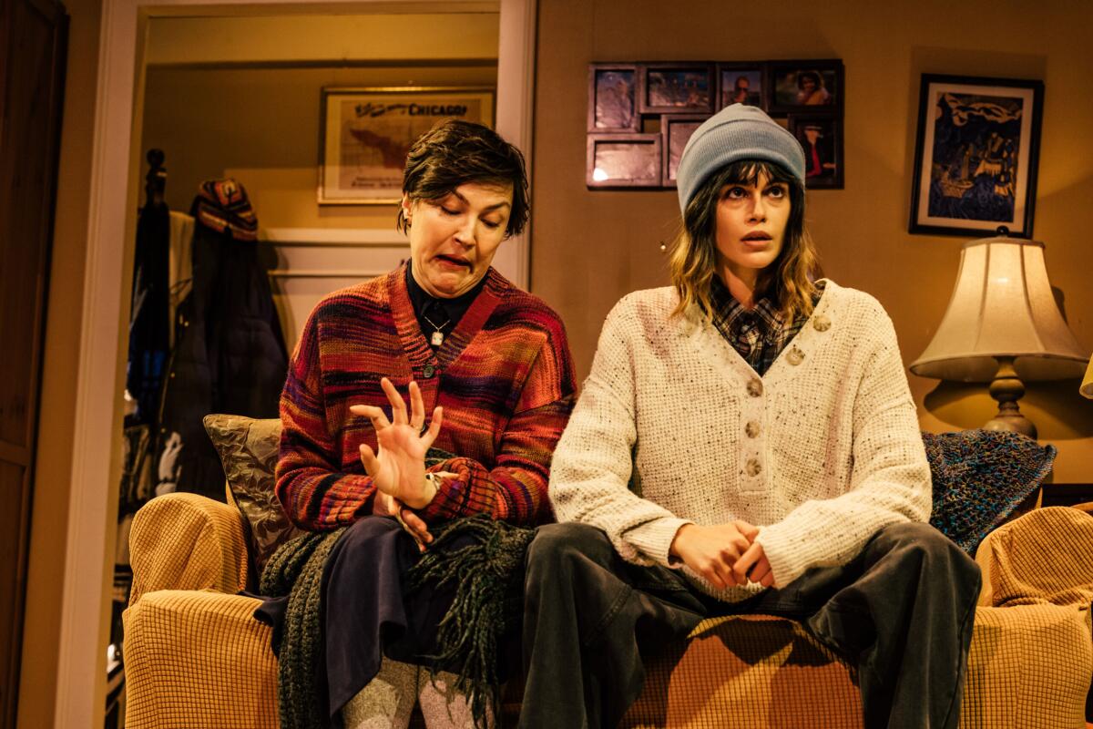 Two women in warm sweaters sit in a living room on a couch.