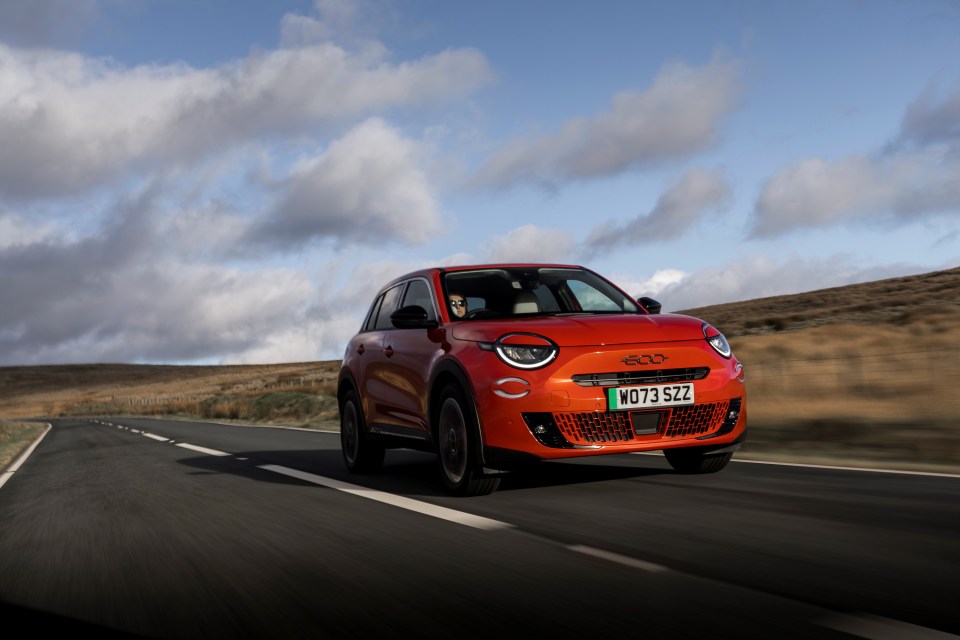 Orange Abarth 500e driving on a road.