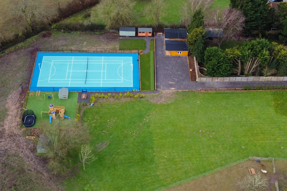 Aerial view of a tennis court, gym, and playground on a property.