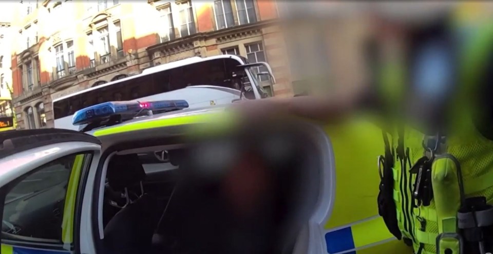 Police officer arresting someone near a bus.