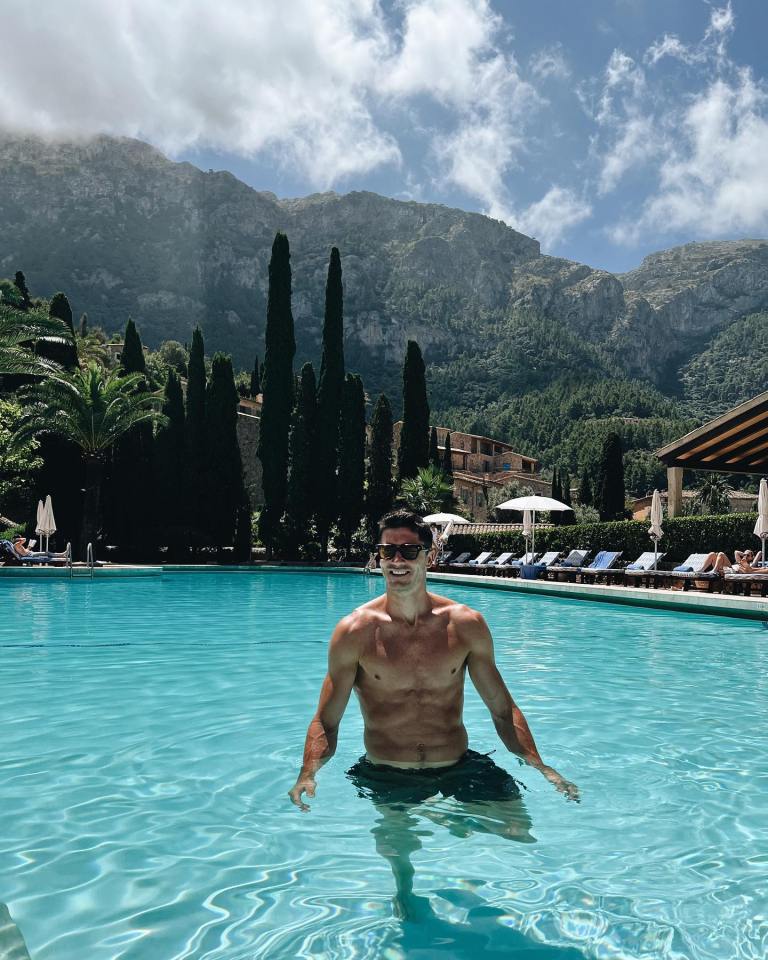 Man in swimming trunks wading in a resort pool with mountains in the background.