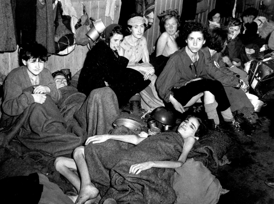 Black and white photo of emaciated women and children huddled together in a cramped space.