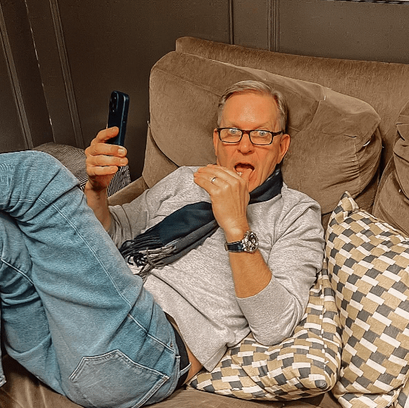 Man on couch looking at phone and eating.