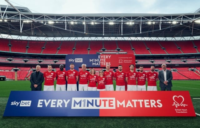 Group photo of people in red shirts standing in front of a banner that says "Every Minute Matters" in a stadium.