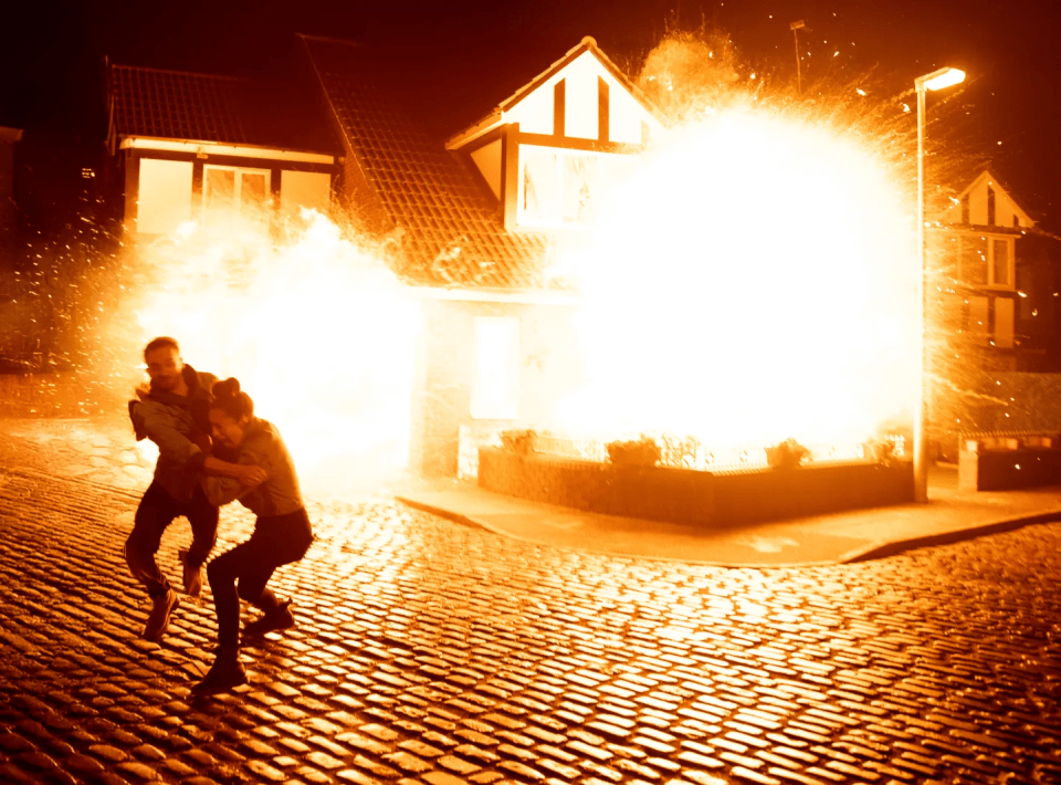 Two people running away from a house explosion.