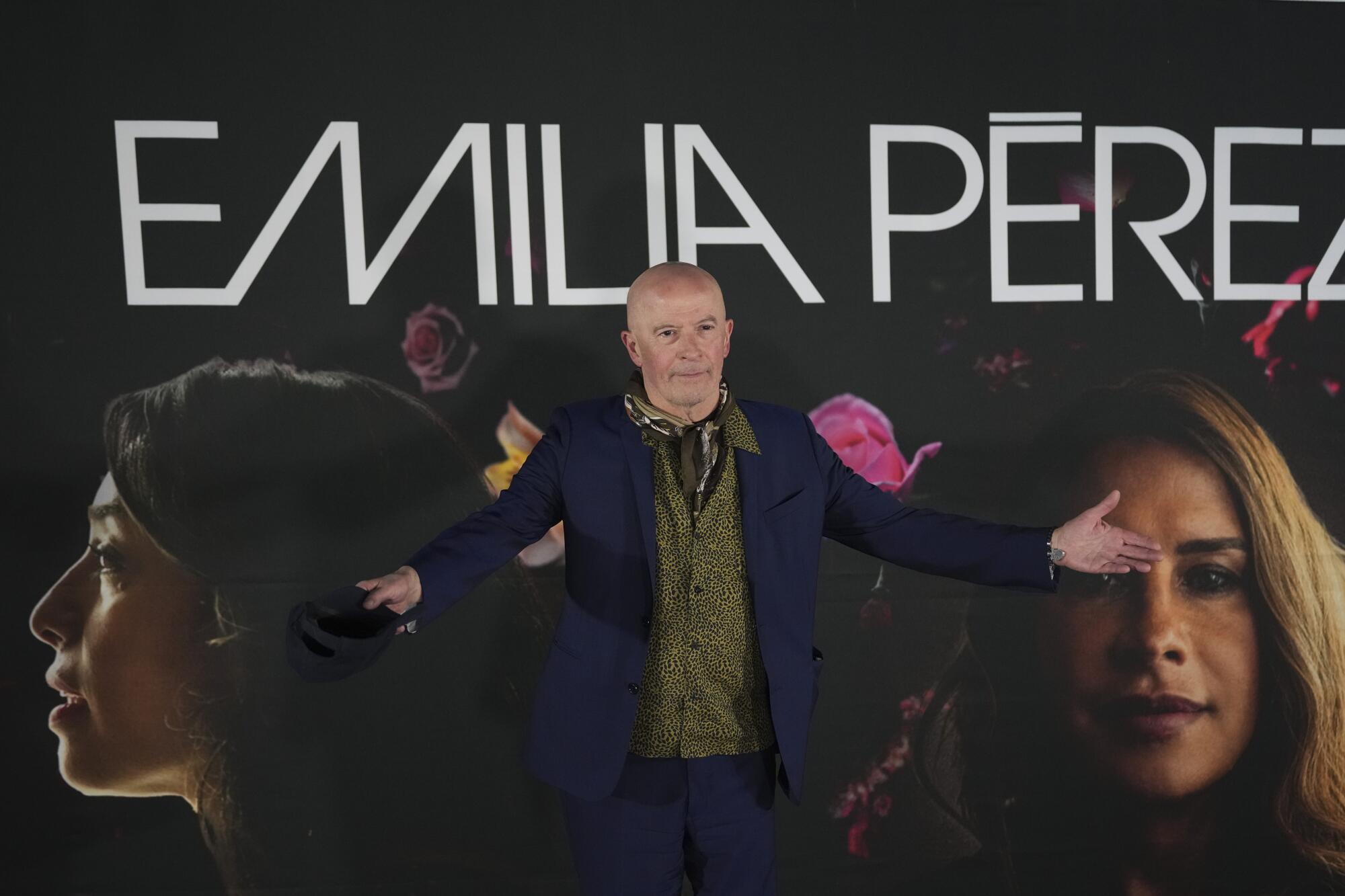 Director Jacques Audiard stands in front of a large wall poster for his film "Emilia Pérez"