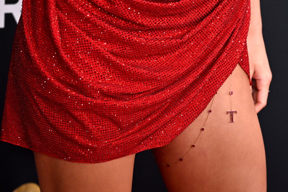 Taylor Swift wearing a red sequined dress and a body chain with a "T" pendant.