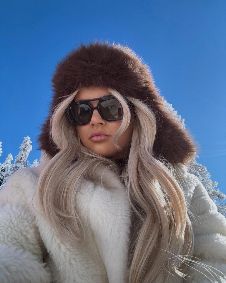 Woman in a fur hat and coat wearing sunglasses in the snow.