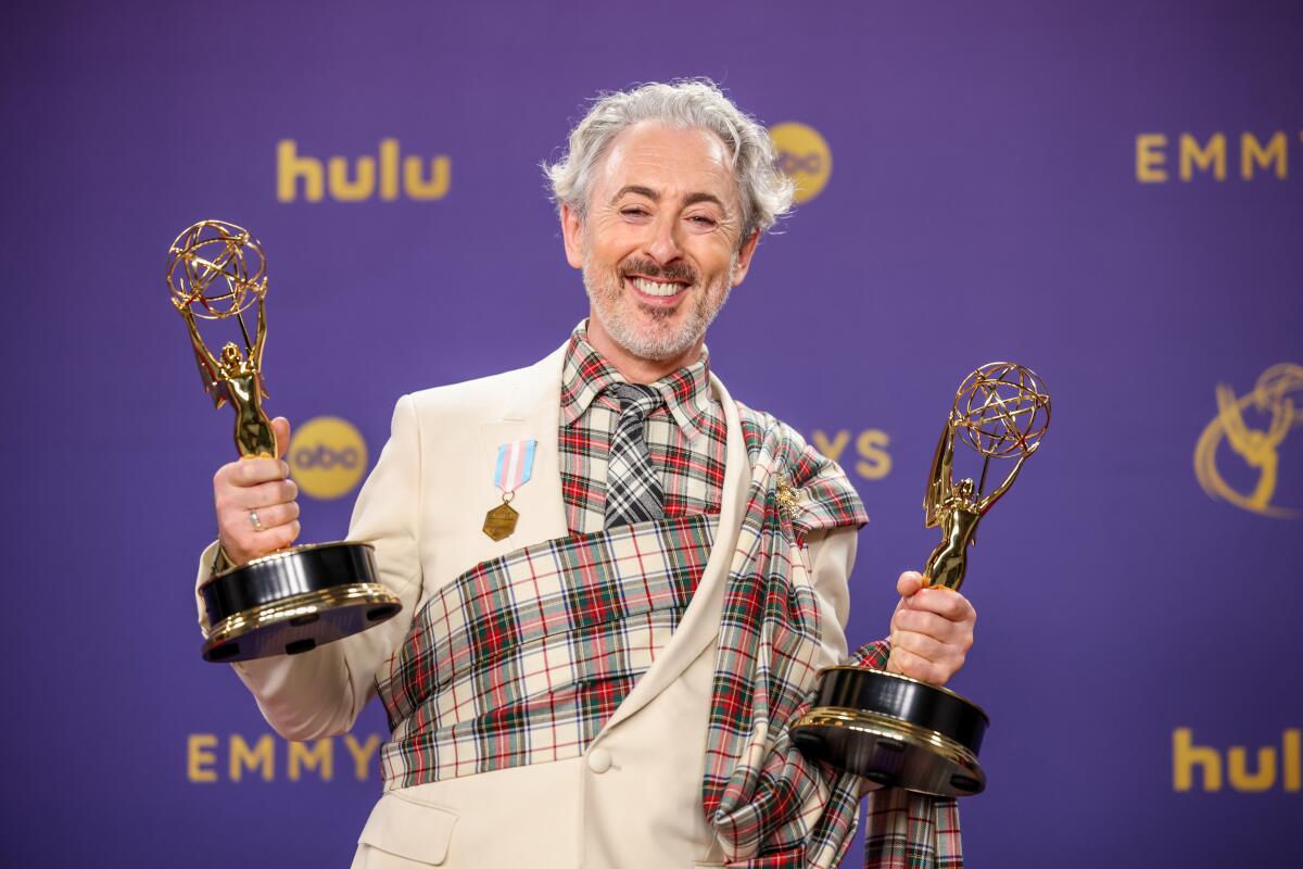 "The Traitors" host Alan Cumming holding a couple of the show's Emmy Awards.