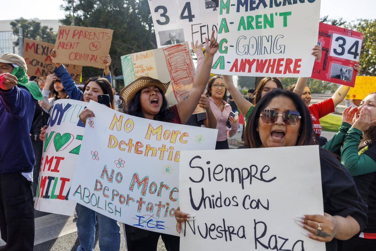 People at a demonstration hold up signs, one of which says No More Detention, No More Deportation