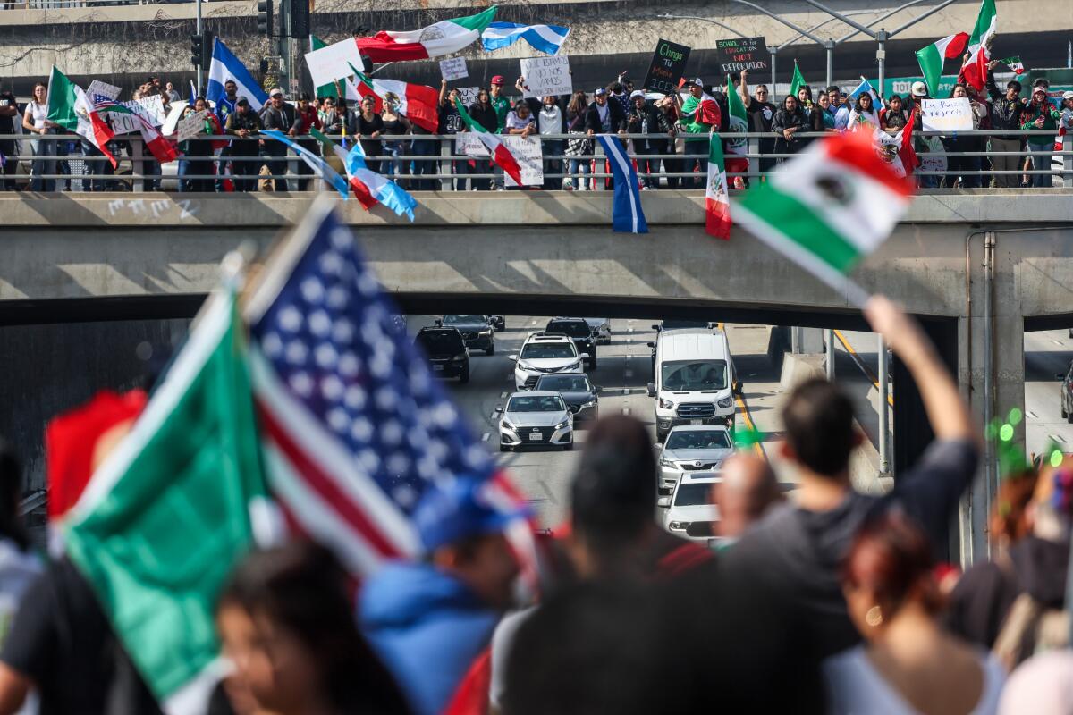 Crowds gather on a freeway overpass while holding U.S. and Mexico flags