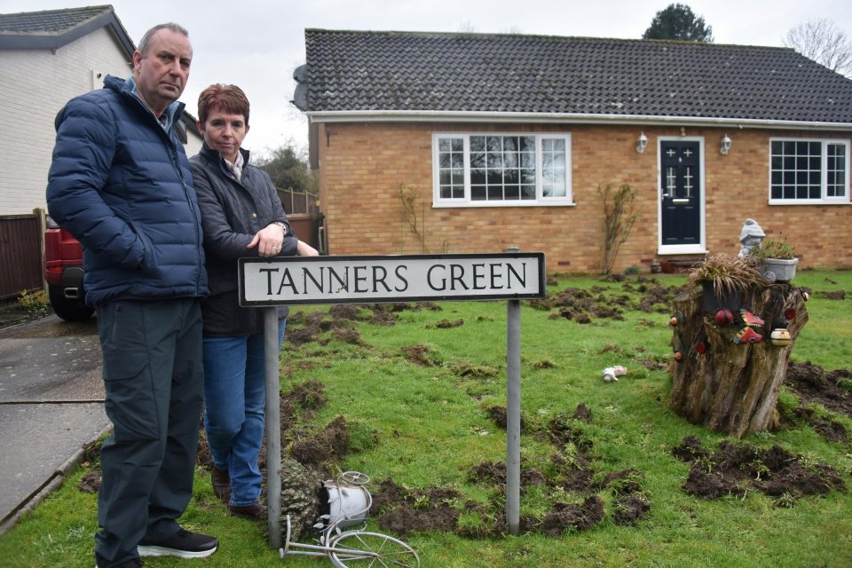 A couple stands in front of their house on Tanners Green, where the lawn has been dug up by pigs.