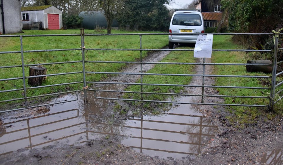 Muddy puddle reflecting a metal gate and a van in a driveway.